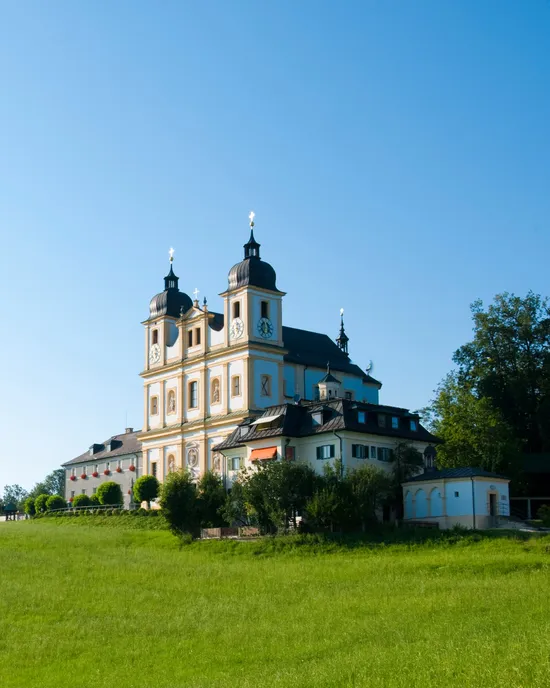 Barockkirche mit Zwillingstürmen auf grasbewachsenem Hügel unter klarem Himmel